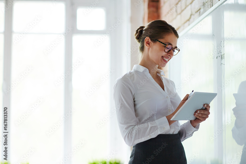 Young teacher with notepad standing by whiteboard in classroom