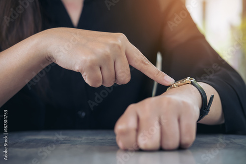 A business woman pointing at a black wristwatch on her arm in working time while waiting for someone with feeling angry