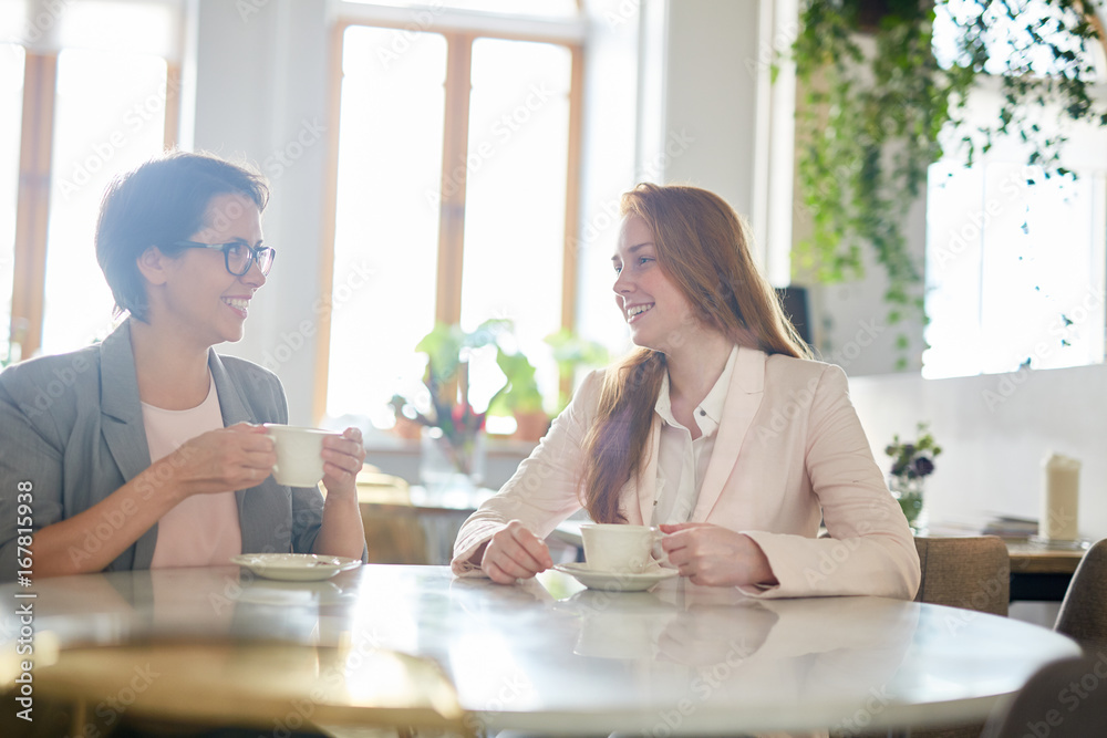 Cheerful white collar workers chatting animatedly with each other while having coffee break, interior of lovely cafe on background