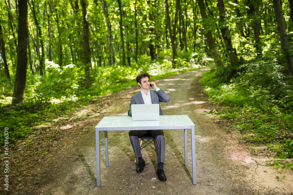 Businessman sitting at the office desk work at laptop computer in green forest park. Freelancer working on office table in green park. Business portrait.