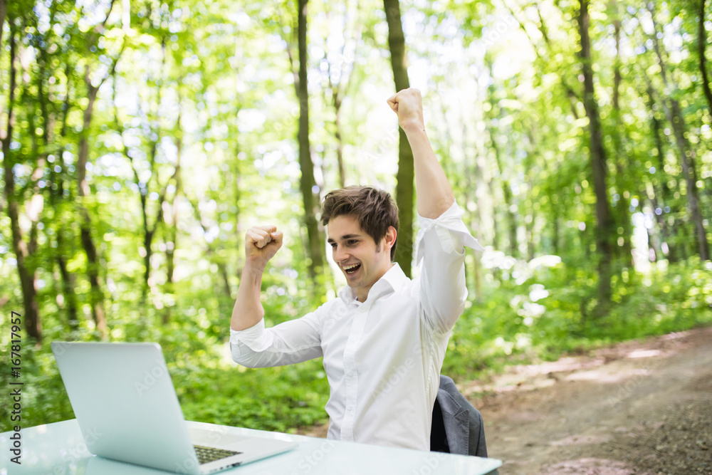 Happy exited business man with raised hands up celebrate new deal with costumer or great news in front of laptop at office desk in green park. Business concept. Happy exited business man with raised hands up celebrate new deal with costumer or great news in front of laptop at office desk in green park. Business concept.