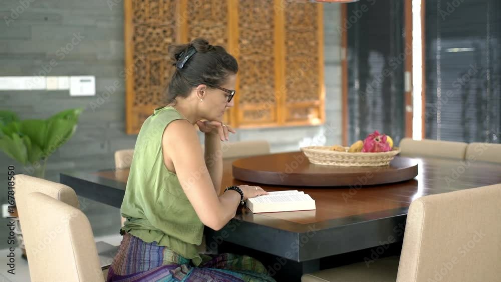 Woman sitting by the table in the dining room and reading absorbing book, steadycam shot
Woman sitting by the table in the dining room and reading absorbing book, steadycam shot