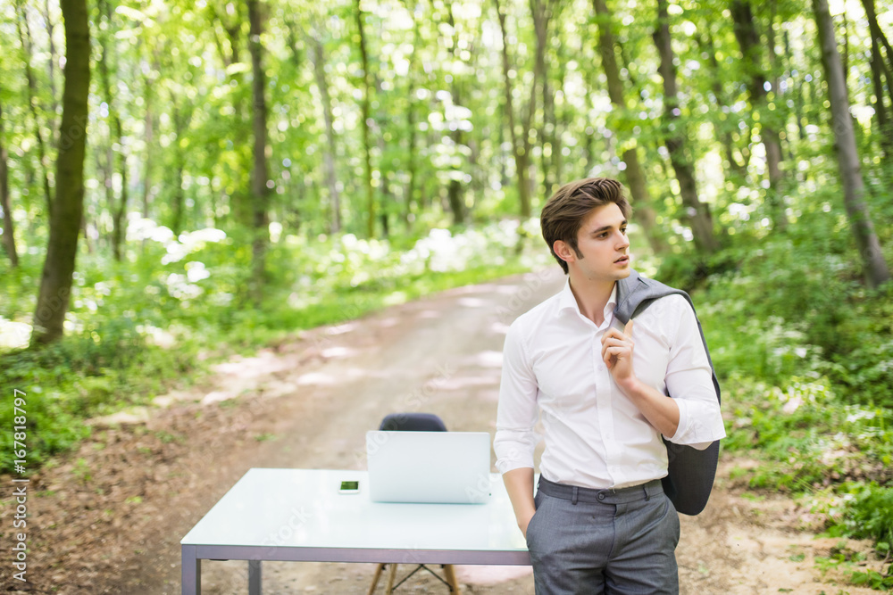 Handsome business man in suit in front of his office desk in green park. Business concept.