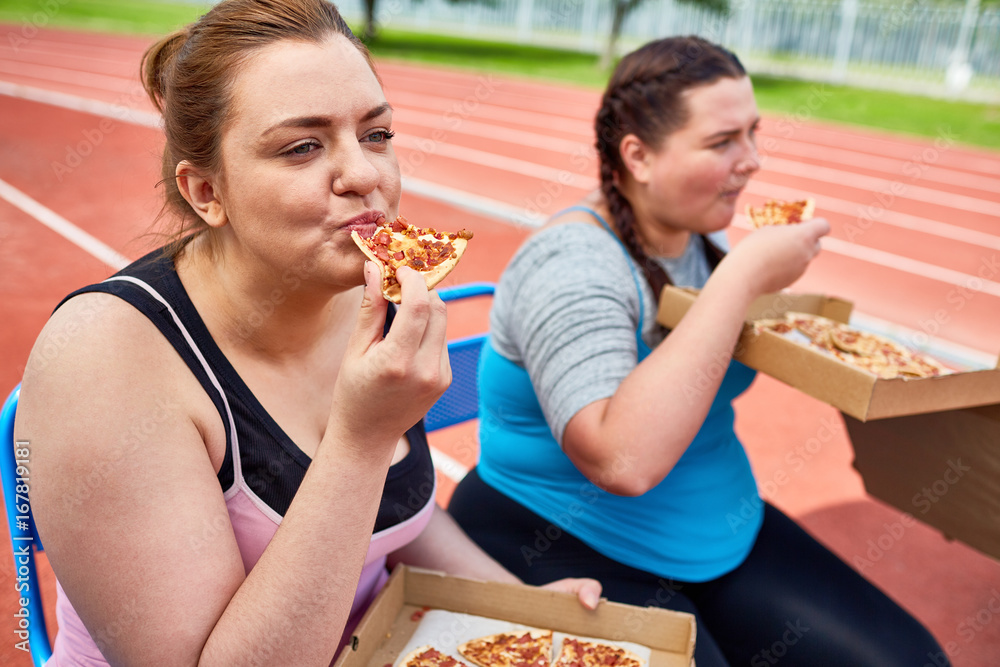 Hungry over sized females eating pizza after workout on stadium Stock Photo Adobe Stock