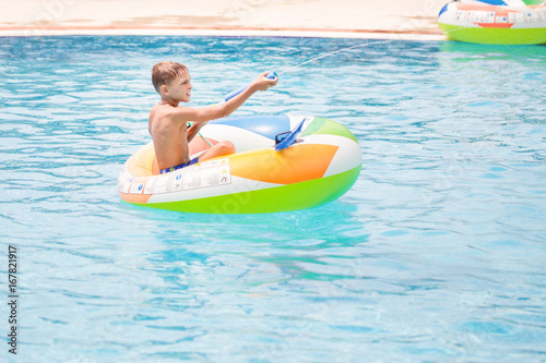 Little boy sitting in inflatable boat and having fun with water gun