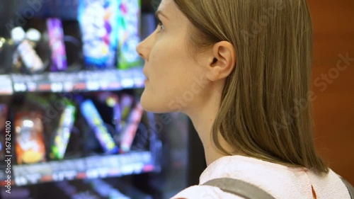 Beautiful hungry woman picking item out of vending machine in mall. Choosing unhealthy snacks being famished