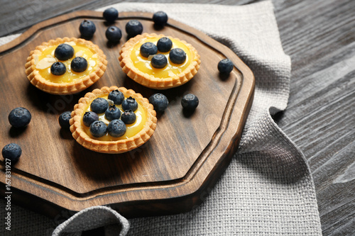 Delicious crispy tarts with blueberries and custard cream on wooden board
