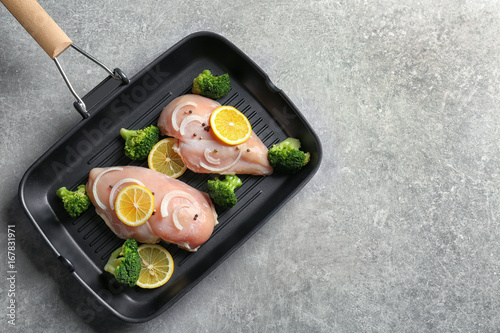 Frying pan with raw chicken breasts, lemon and broccoli on table