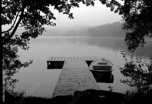 BW photo of pier with boat at foggy morning