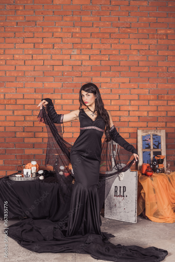 Naklejka premium sexy girl in costume of witch.Halloween decorations with spiders and pumpkin bucket for trick or treat. Greeting Card.Halloween pumpkin brick background.Happy Halloween postcard. Ideas for Halloween. 