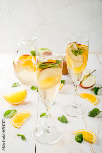Drinks and cocktails. White autumn sangria with apples, orange, mint and white wine. In glasses for champagne, in a pitcher, on a white wooden table. Copy space
