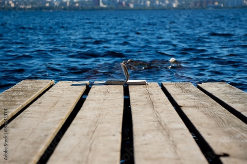 The book lies on the edge of the pier, on a wooden surface against a clear lake