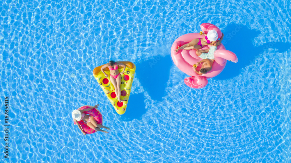 AERIAL TOP DOWN Relaxed girls and guys lying on fun colorful floaties floating on pool water. Happy smiling friends enjoying summer vacation chilling on inflatable pizza, flamingo and doughnut floats