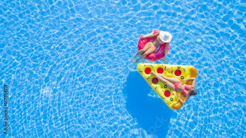 AERIAL TOP DOWN Relaxed girls in pink bikini swimsuits lying on fun inflatable pizza and flamingo floating loungers on water. Girlfriends on summer vacation enjoying colorful floaties in swimming pool