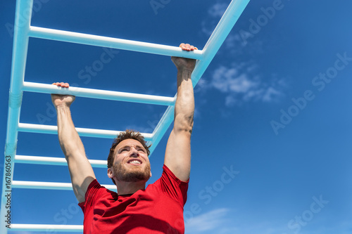 Fitness monkey bars man training arms muscles on jungle gym outdoors in summer. Athlete working out gripping climbing on ladder equipment at sport athletics centre.