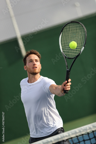 Tennis player man hitting volley with forehand returning ball playing on court. Athlete portrait training on summer practice.