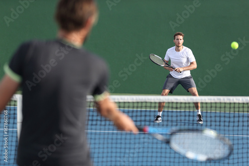 Men sport athletes players playing tennis match together. Two professional tennis players hitting ball on hard outdoor court during game.