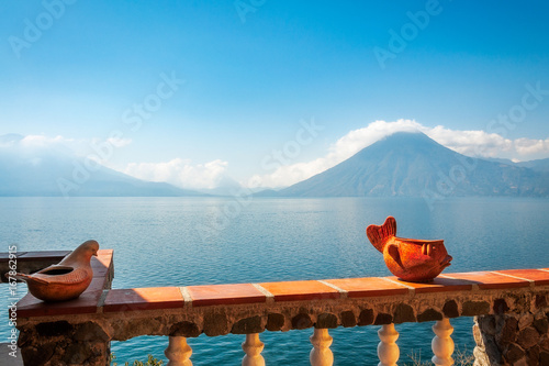 Hazy view of the blue waters of Lake Atitlan in the morning from a sunny terrace with some interesting ceramic decorations. In the background we can see the volcanoes San Pedro and Toliman. photo