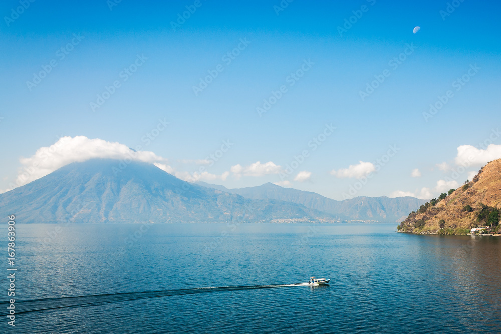 Moon rising at lake Atitlan in Guatemala, with San Pedro Volcano in background and a small tourist motor-boat in foreground.