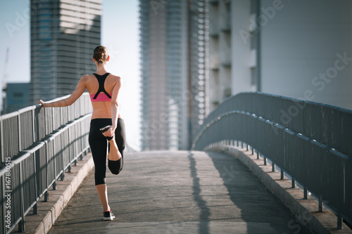 Female runner on city bridge warning up before run.