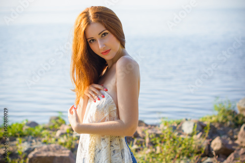 Tender beautiful red hair lady at evening sunlight around rocks and sea water. Woman wearing in lace cardigan. Portrait in vintage style on vacation. Girl relax at warm day