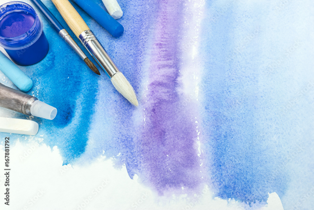 Fototapeta premium paintbrushes with paint and pastel crayons on blue watercolor background with paper texture