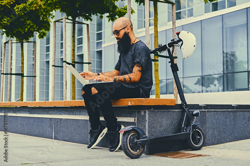 Bearded male using a laptop after electric scooter ride.