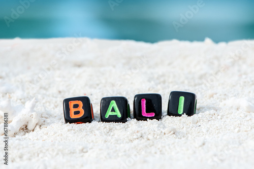 Word Bali is made of multicolored letters on snow-white sand against the blue sea. Tourism, rest, resort, sea, sun, beach 