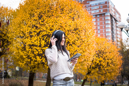 Happy teen woman listening to music and relax in autumn park. Yellow trees  beautiful fall time