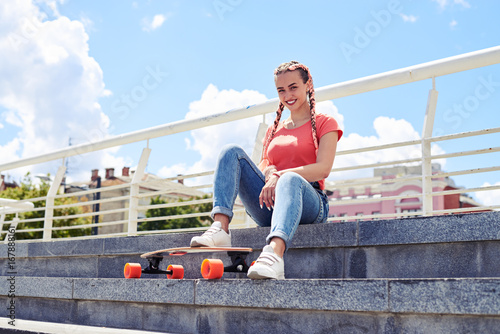 Cheerful girl having rest on stairs after riding skateboard
