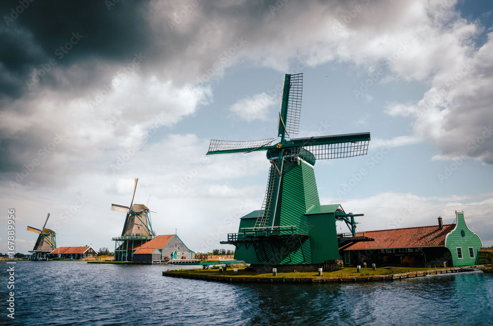 View of Authentic Zaandam mills in Zaanstad village on the river Zaan against the stormy sky with clouds. Landmark of Netherlands.