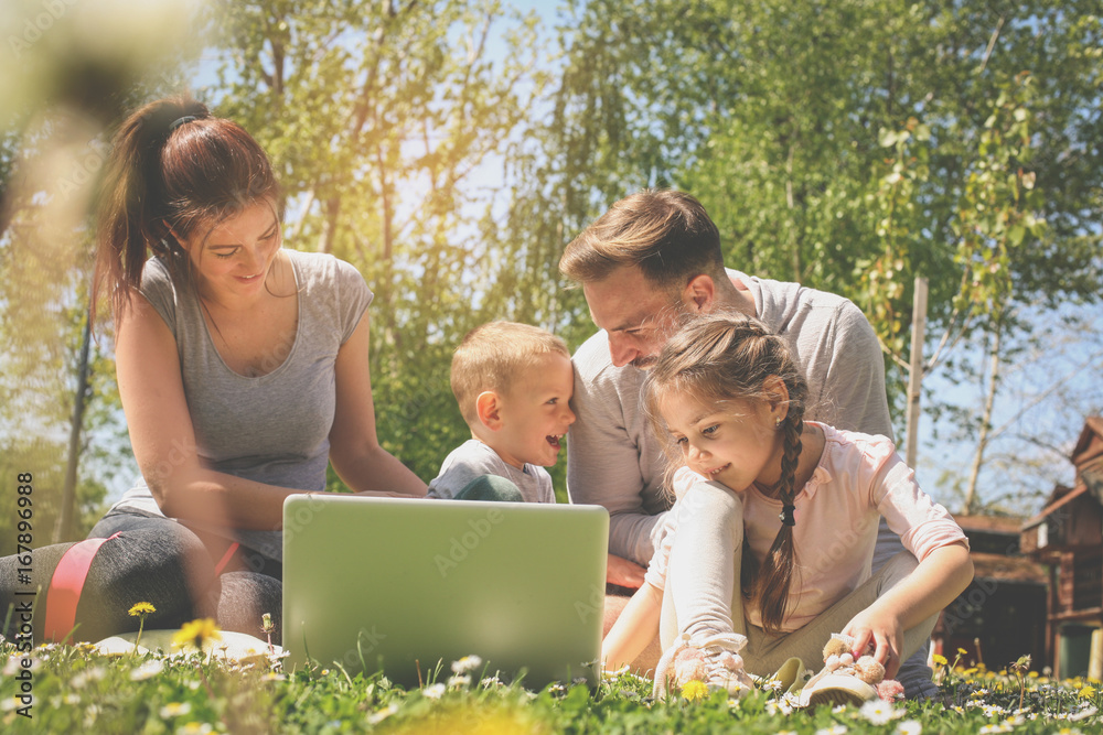 Happy family using laptop, sitting on the green grass. Family enjoying on the meadow in the spring day. Happy family using laptop, sitting on the green grass. Family enjoying on the meadow in the spring day.