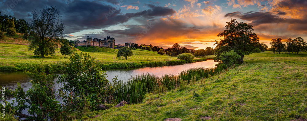 Fototapeta premium Panoramiczny zachód słońca nad rzeką Aln / Rzeka Aln biegnie przez Northumberland od Alnham do Alnmouth. Widziany tutaj w panoramie poniżej Alnwick Town i Castle na panoramie, jak zachody słońca