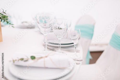 Roll of white serviette decorated with green branch lies on a dinner plate © myronovychoksana