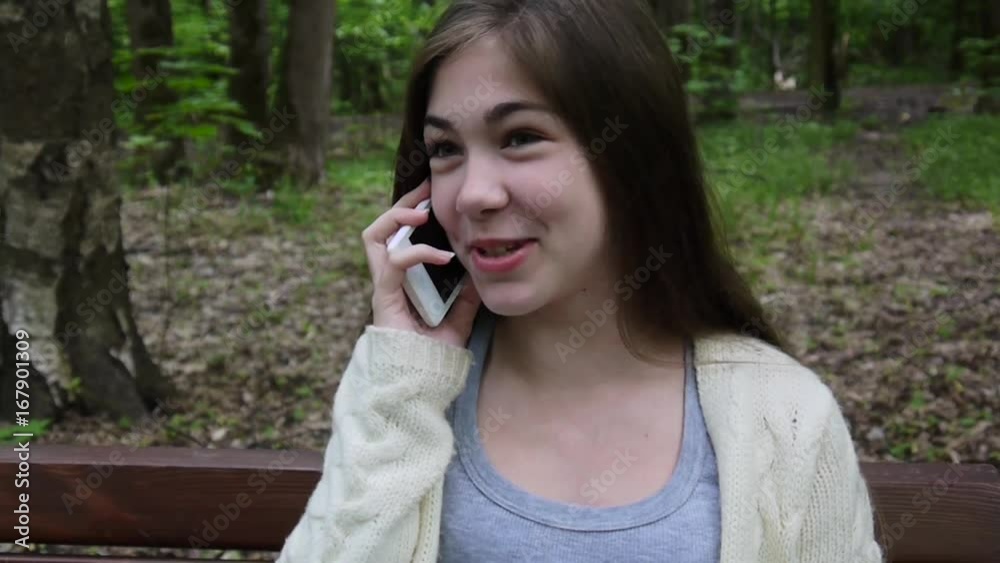 Young attractive girl speak to phone on bench. Summer park. Smile. HD video footage shooting static camera. Young attractive girl speak to phone on bench. Summer park. Smile. HD video footage shooting static camera.