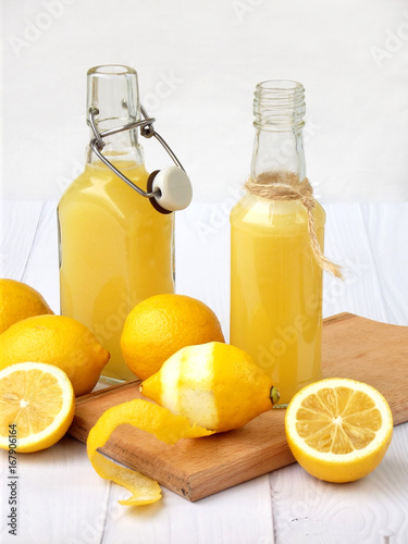 Freshly squeezed lemon juice in bottle and lemons on light background. For vitamin drink or cocktail. Selective focus. Space for text.