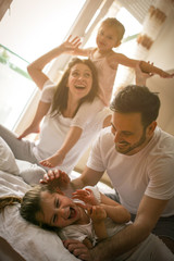 Cheerful family playing together on bed. Parents spending free time with their daughters.