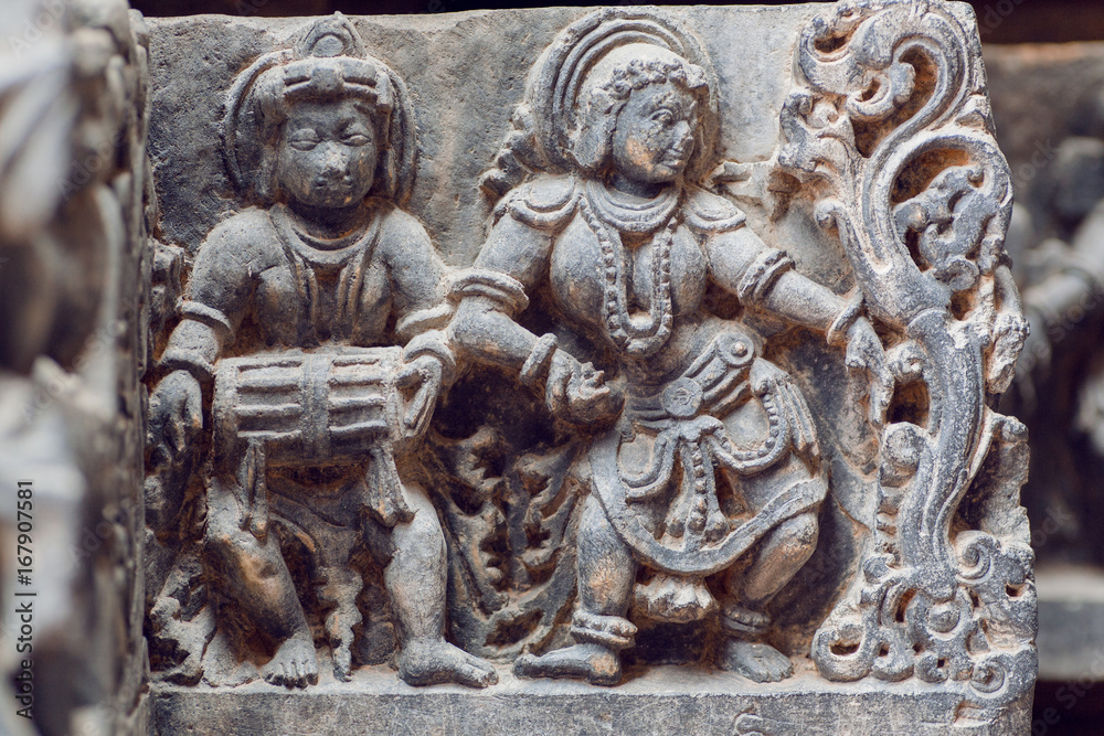 Indian architecture background on traditional style relief, with drummer musician and dancing woman inside the 12th century Hoysaleshwara temple in Halebidu, India.