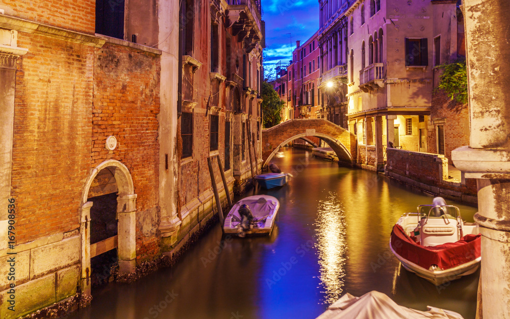 Venice at night with boats on canals, lights and typical Venetian buildings.