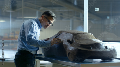 Chief Automotive Designer with Rake Sculpts Futuristic Car Model from Plasticine Clay. He Works in a Special Studio Located In a Large Car Factory.