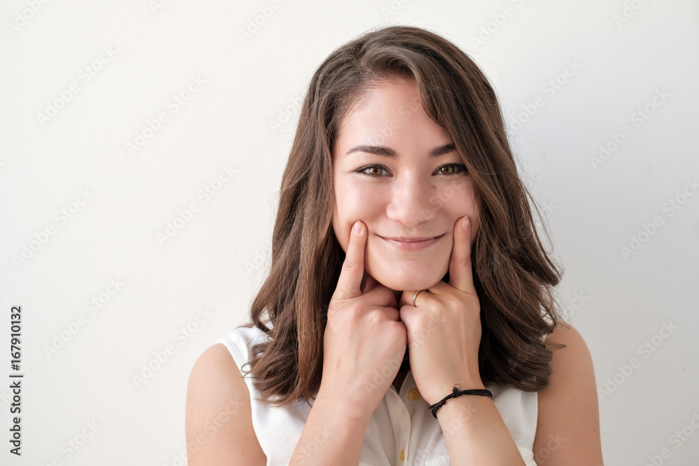 Close up shot of beautiful teenage girl forcing a smile, holding her fingers near lips, looking with happy expression Close up shot of beautiful teenage girl forcing a smile, holding her fingers near lips, looking with happy expression