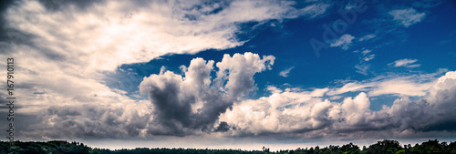 Panorama from aerial photos of a cloudy blue sky with strong clouds above a forest