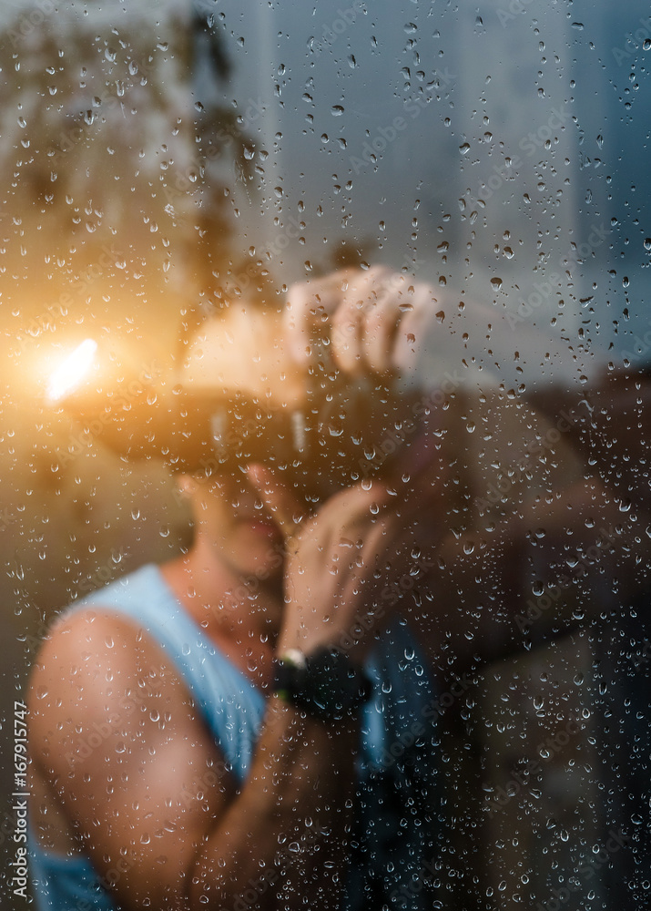 A man is standing behind a glass, and on the glass a drop of rain