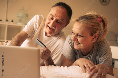 Senior couple lying in bed and buying over the Internet by credit card.