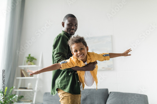 afro father and son playing at home, pretending airplane