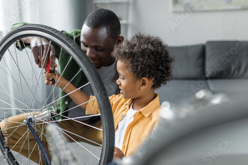african-american father and son repairing wheel of bicycle