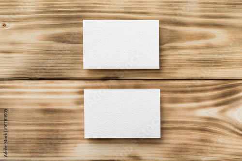 Closeup mockup of two white blank horizontal business cards at light natural wooden background.