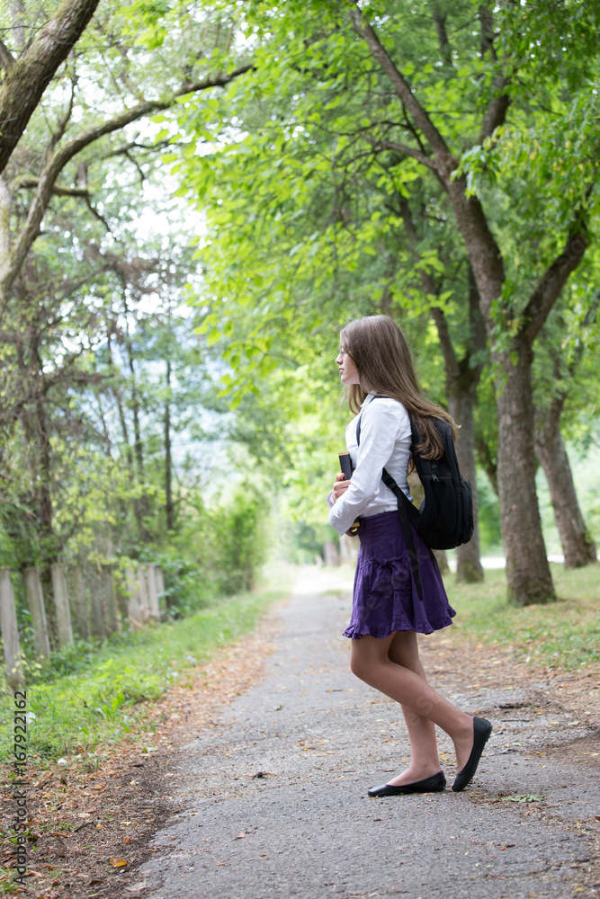 Pretty beautiful blonde school girl child with glasses, white shirt, purple skirt and backpack holding notes and books standing in the nature alley back to school autumn Pretty beautiful blonde school girl child with glasses, white shirt, purple skirt and backpack holding notes and books standing in the nature alley back to school autumn