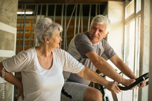 Two senior people at the gym. Senior man sitting on the elliptical machine and having conversation with senior woman.