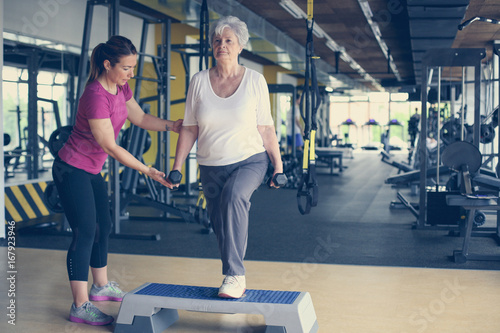 Personal trainer working exercise with senior woman in the gym. Senior woman lift weight.